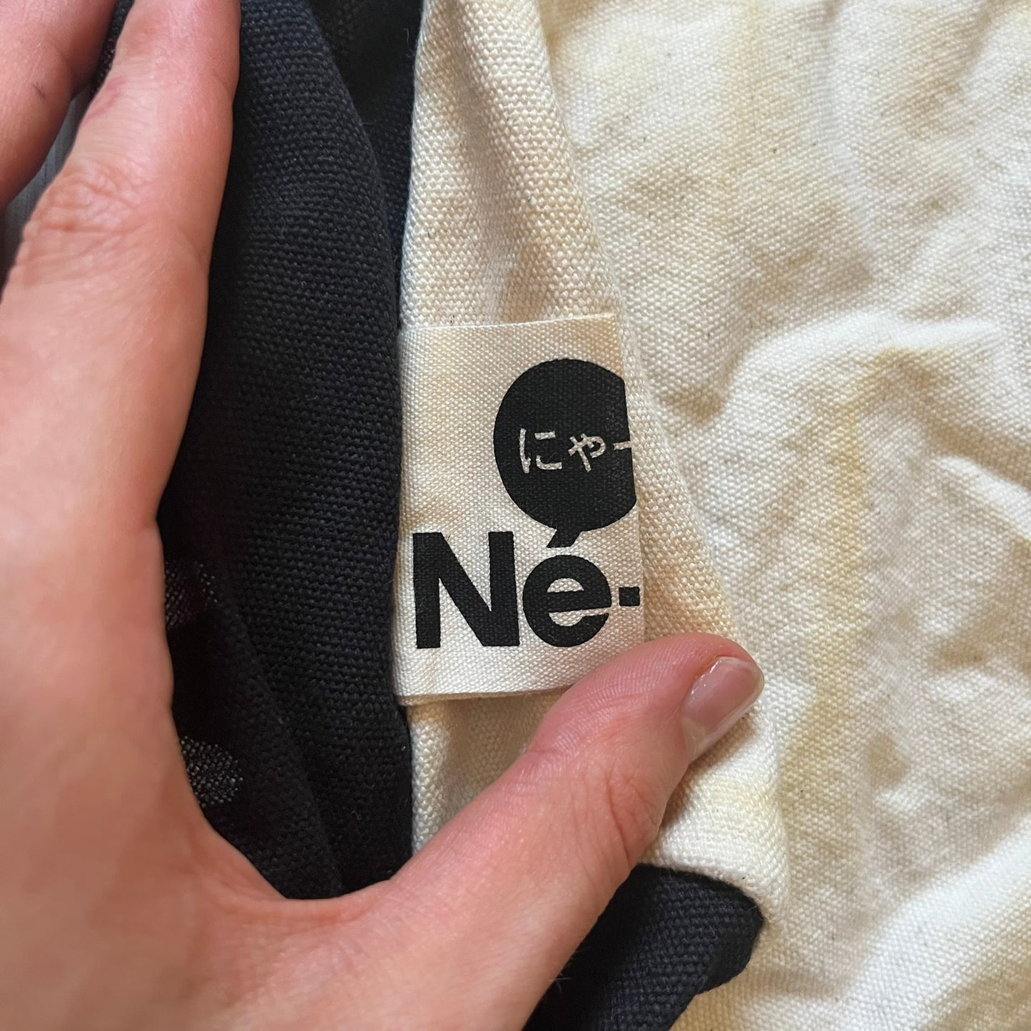 Close-up of a label on a garment with text and a logo, held by a hand.