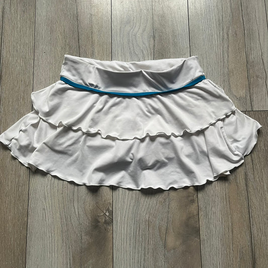 Nike Active Frilly 00’s Tennis Skirt is a women’s tennis skort with integrated inner shorts for support. The white skirt features multiple irregular frilly layers, creating a layered look, with a blue embroidered Nike Swoosh on the front layer. A blue contrast line separates the waistband from the skirt, emphasizing its sporty 2000s design.