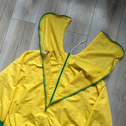 Nike Brazil Olympics Split Windbreaker from 2008, created by designer Jarrett Reynolds. Crafted in yellow with green hems and zippers. Blue circle and white Nike embroidered logo on the chest. This innovative jacket can be zipped apart on both sides and merged with other compatible models. Hidden inside, a small Brazil flags accent completes the concept.