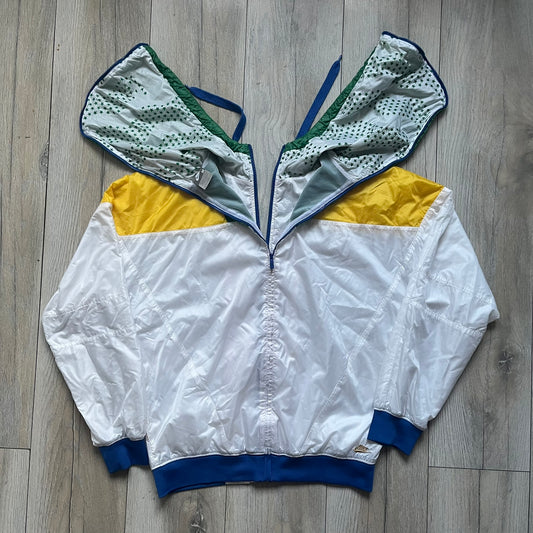 Nike Brazil windbreaker released in 2008 to mark the 50th anniversary of Brazil’s football legacy. Features a split color-block design with white lower panels and sleeves, yellow and green upper section, blue cuffs and hems, and a green hood. Detailed with a gold embroidered Nike logo on the chest, a gold-tone metal Brazil crest pin on the opposite side, and “1958-2008” with a “50” printed on the hood. The hood interior is white with an all-over green star pattern.