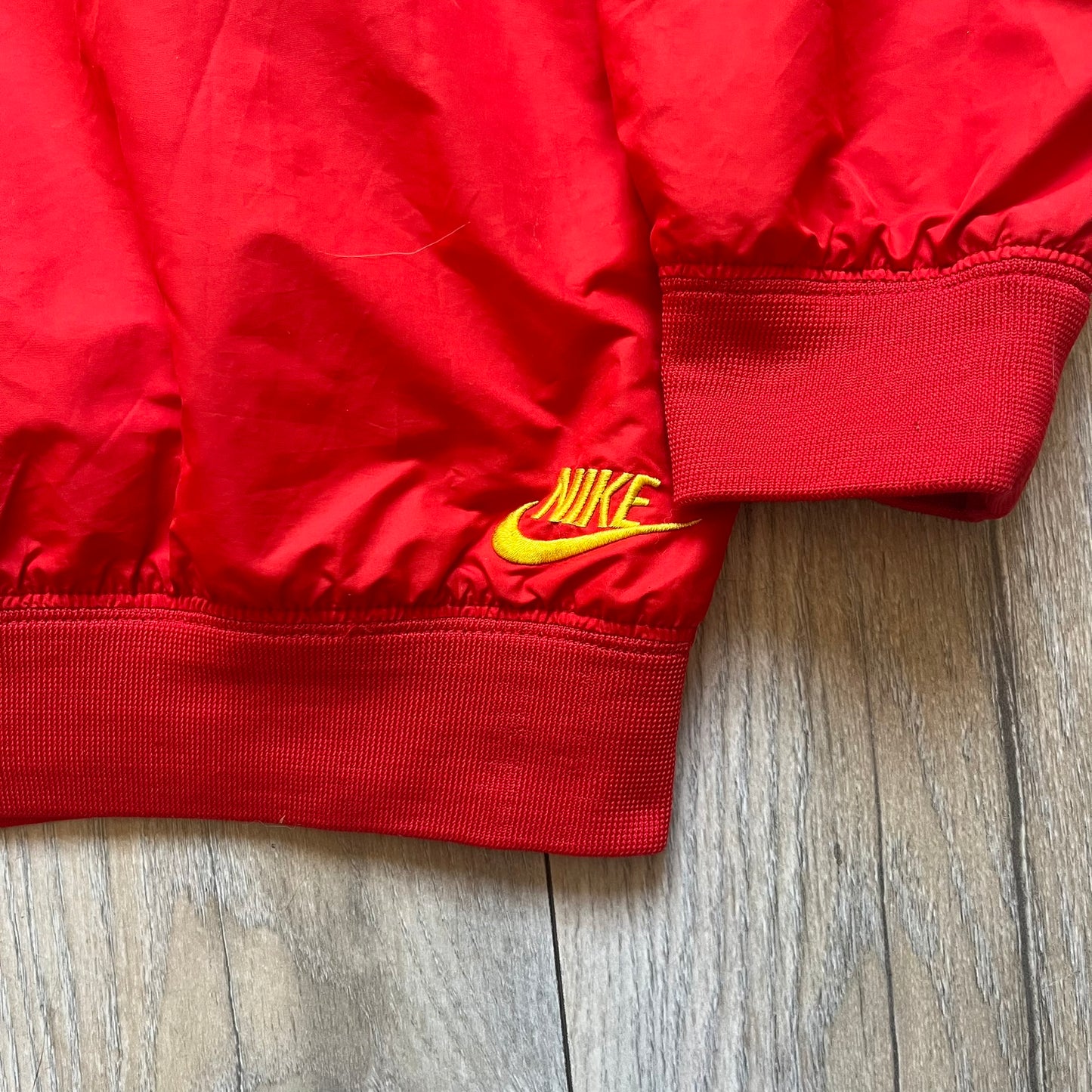 Nike China Olympics Split Windbreaker from 2008, crafted in red with a yellow hood representing China colors. The chest features embroidered yellow Nike logo and China flag stars on the other side. This innovative jacket can be zipped apart on both sides and merged with other compatible models. This jacket doesn't have typical flags in the pockets.