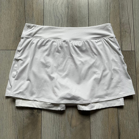 Nike Court Victory W Tennis Skirt is a women’s tennis skort with built-in inner shorts for coverage. The skirt is white with a Nike Swoosh at the lower hem and features a triangular cutout detail next to the logo for added mobility.