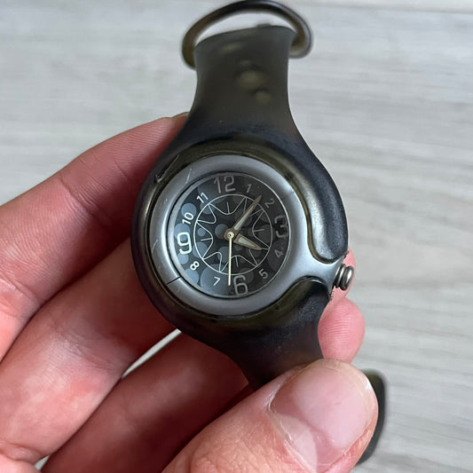 A minimalist timepiece from Nike, the Jelly Bean WK0003 stands out with its transparent dark strap filled with intentional bubble accents. The small analog face continues the theme with subtle grey bubble details, creating a sleek and unconventional design.