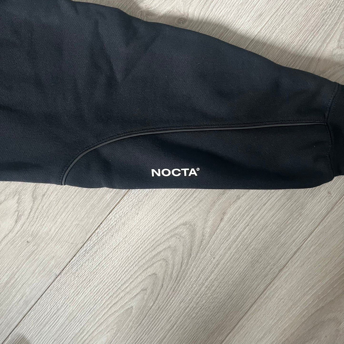 Nike x Nocta Fleece CS Hoodie in Black combines Drake’s refined streetwear vision with Nike’s premium craftsmanship. Made from an ultra-soft fleece blend, it features reflective piping, a silicone Swoosh logo and discreet NOCTA branding. With an adjustable hood, kangaroo pocket, and hidden zip pocket, this piece balances luxury comfort and technical precision.