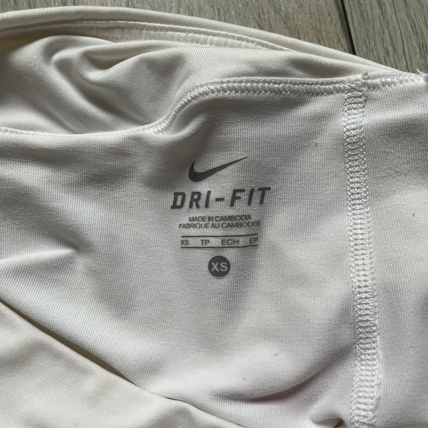 Nike Smash Classic White/Red Tennis Skirt is a women’s tennis skort with built-in inner shorts. The design is constructed in three sections: a white waistband and upper panel, a red middle stripe, and a lower white layer with two cutouts revealing red fabric underneath. A white Nike Swoosh is placed at the lower hem, with a small Nike Court logo on the side.