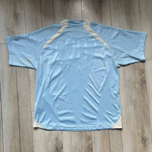 Nike Sphere Dry 90’s Baby Blue Tee is a baby blue T-shirt featuring gray and white stripe detailing. The front includes a dark gray Nike logo alongside a “90” graphic, with an additional Nike logo on the sleeve. The back displays a large light blue “90” print