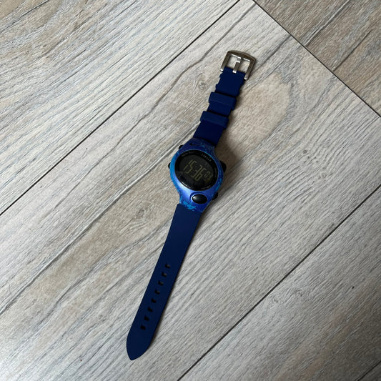 Nike Triax 120 WG40-0010 Digital Watch features a blue case with a black Nike Swoosh above the display and a black control button below it. The watch has a black digital screen with light-colored numerals and is fitted with navy-blue replacement straps that are not original Nike straps. Constructed from stainless steel and plastic materials, it offers 100-meter water resistance, 120-lap memory, and multiple timing and training modes.