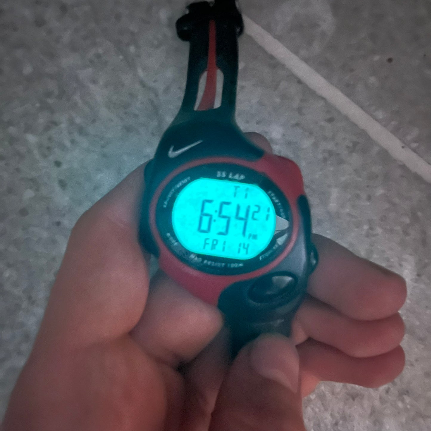Digital stopwatch with Nike logo held in a hand on a concrete floor.