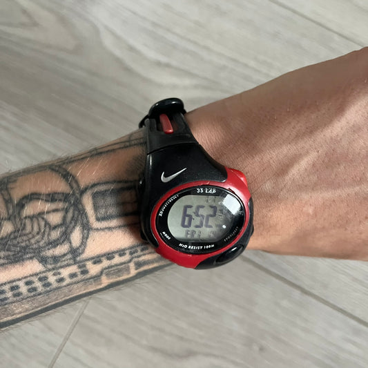 Digital watch with red and black band on a wrist with tattoos
