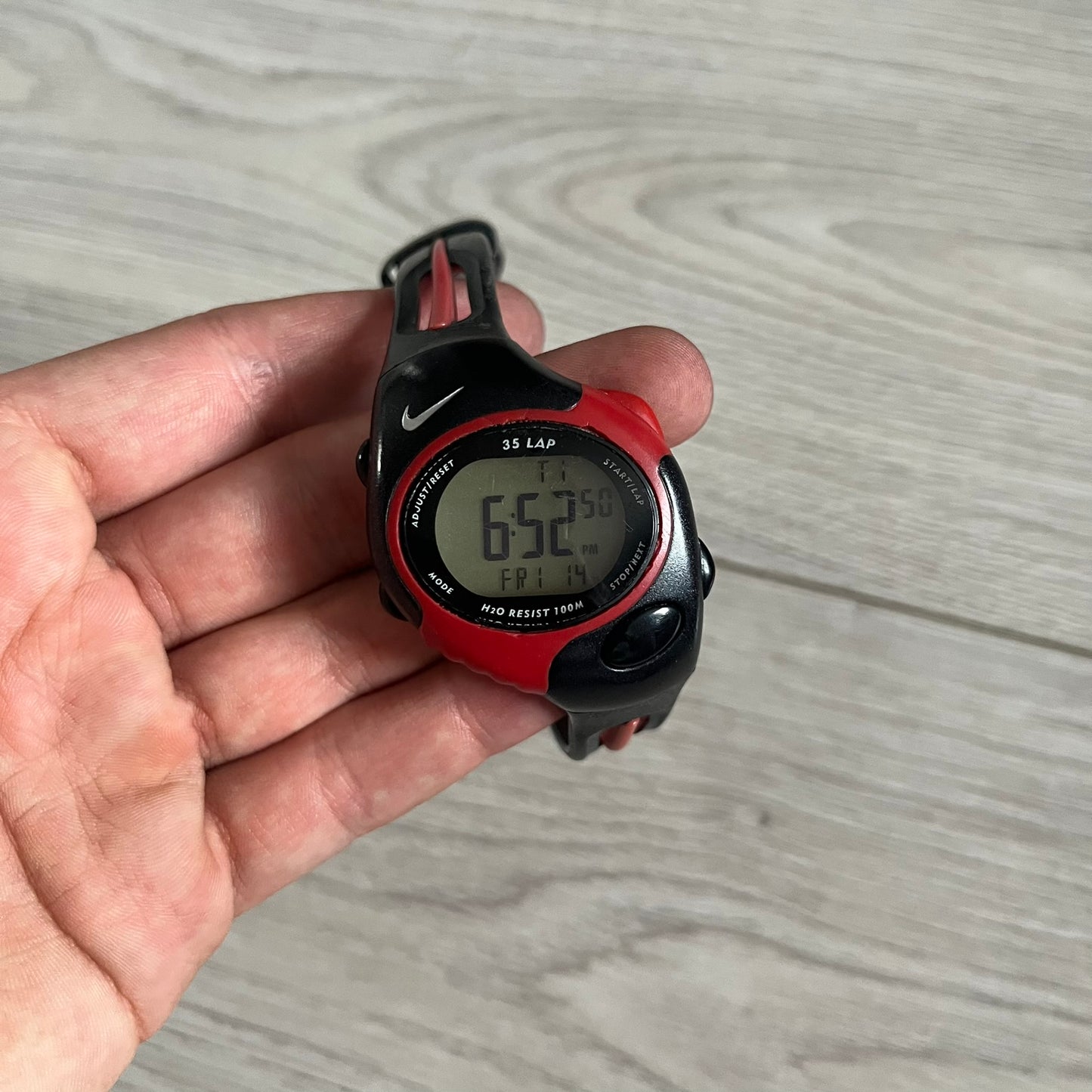 Red and black digital watch held in a hand on a wooden surface