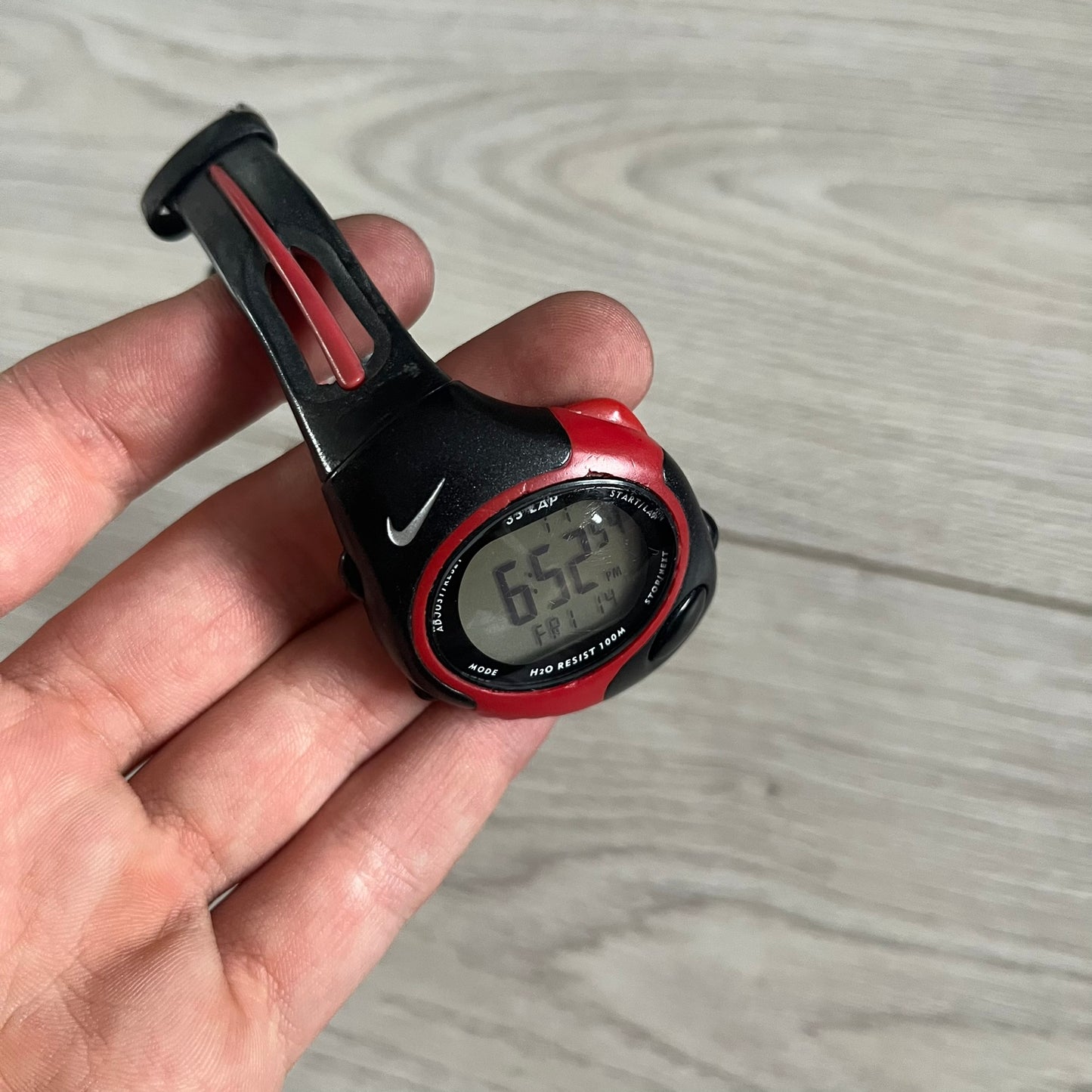 Digital watch with red and black design held in a hand on a wooden surface