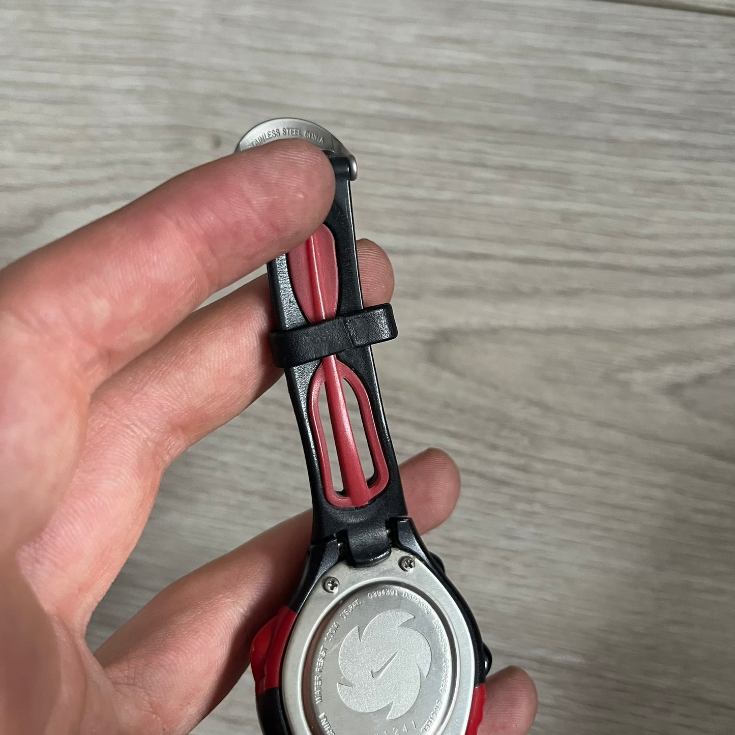 Hand holding a silver and red pocket knife against a wooden background