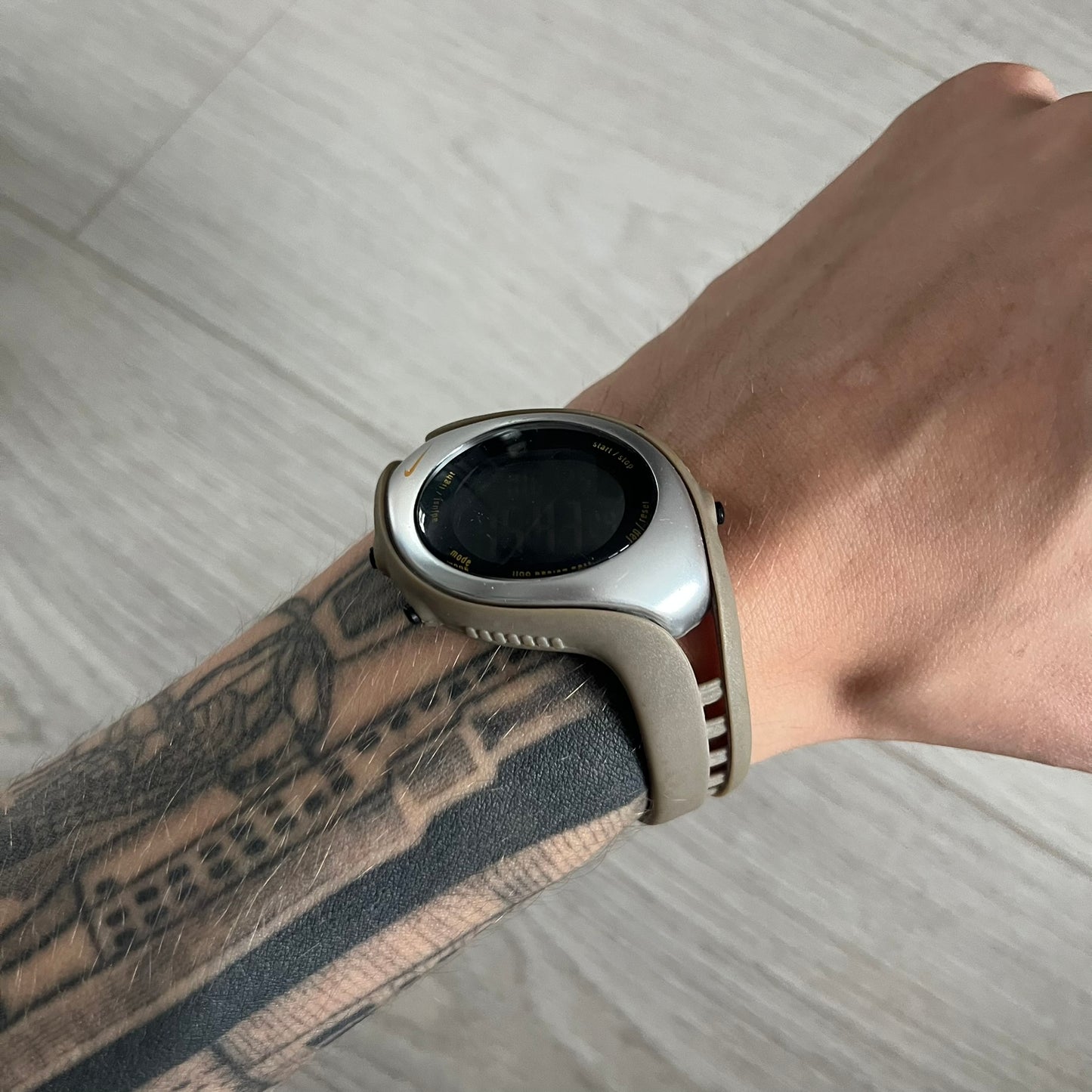 Smartwatch on a wrist with a tattooed arm against a neutral background