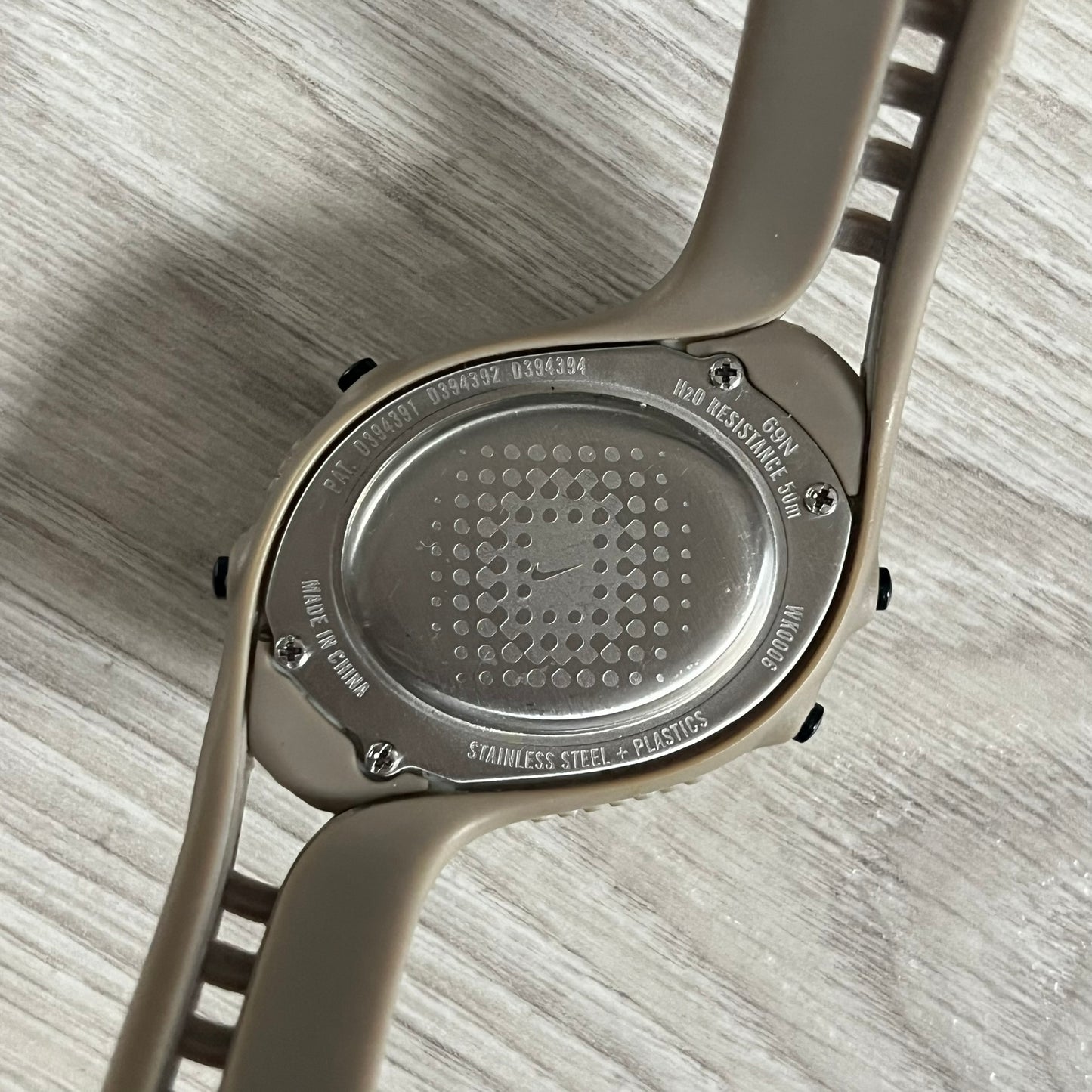 Close-up of a watch case with brand engraving on a light wooden surface