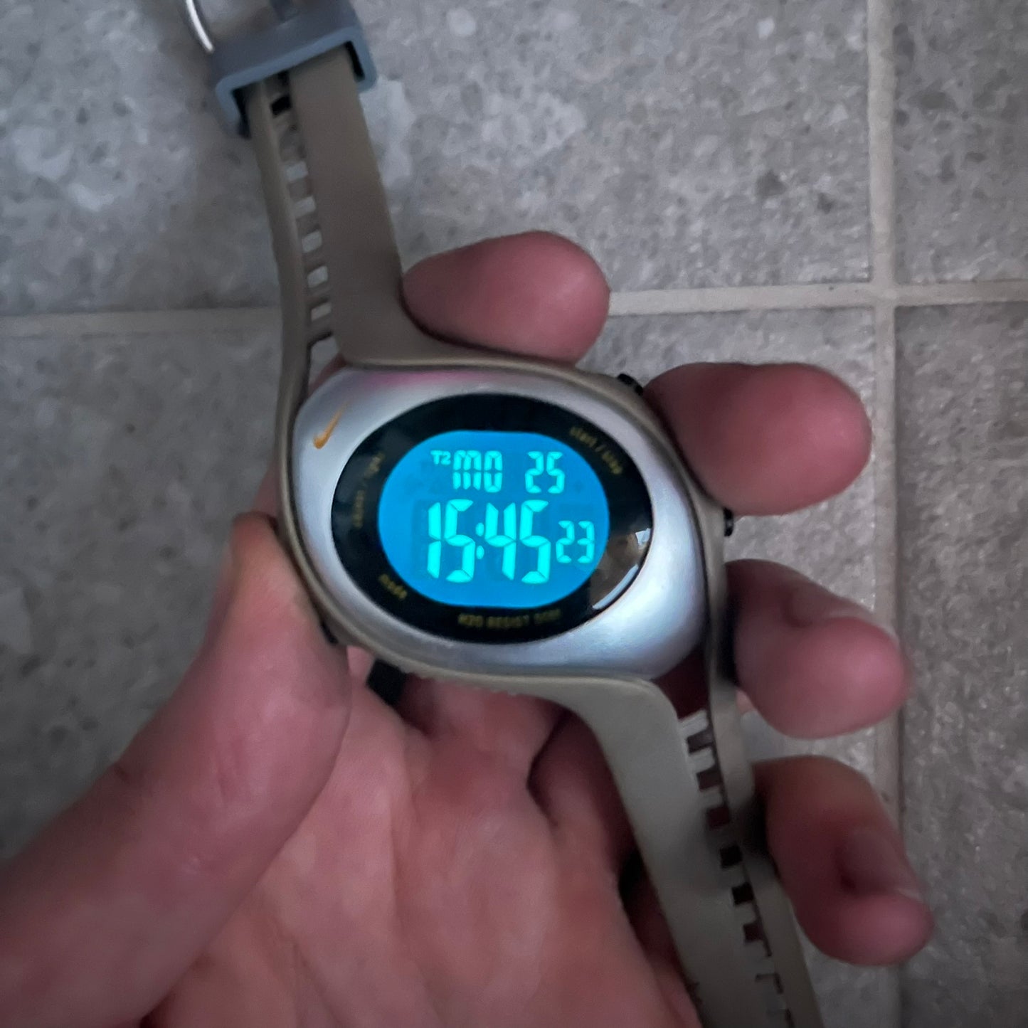 Digital watch held in a hand with a tiled floor background