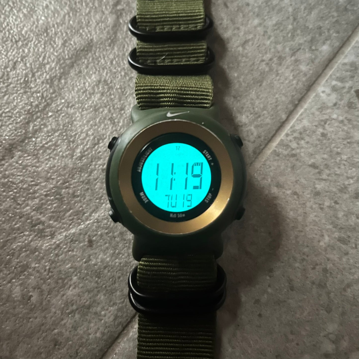 Digital watch with green strap on a gray surface