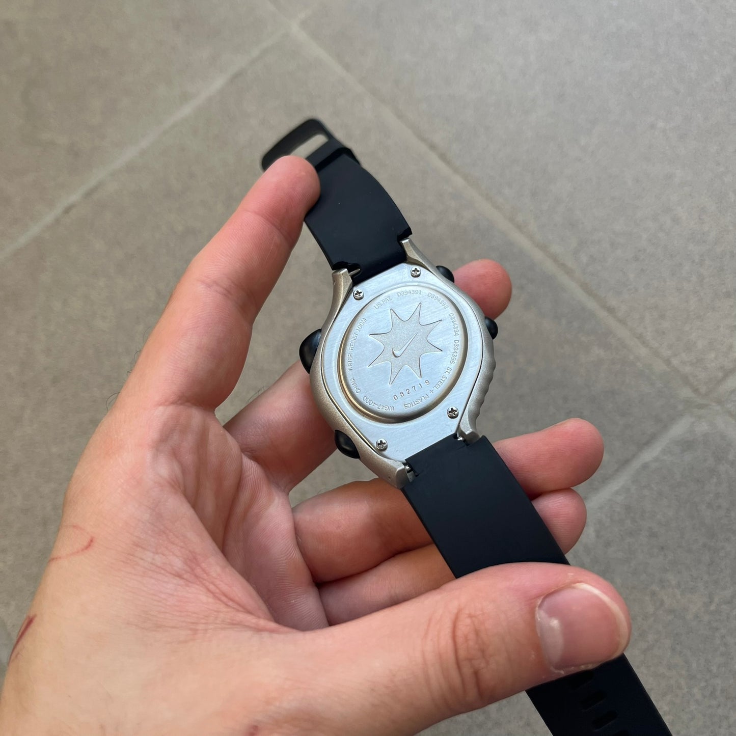 Nike Triax Regular 20 Silver Analog Watch features a silver-tone case with four black side buttons and a front button for the backlight function. The watch has an orange Nike Swoosh on the top of the case, 20-lap memory, multiple modes, and 100m water resistance. It comes with black replacement straps that are not original Nike.