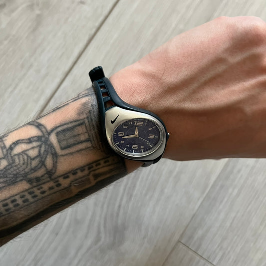 Nike Triax Roar Junior WK0007 analog watch featuring a navy rubber strap with matching navy case sides and a silver-tone front case. The metallic blue dial has a high-shine finish, silver hour markers, and silver hands for clear visibility. Built with stainless steel and metal components, the watch is water resistant up to 50 meters