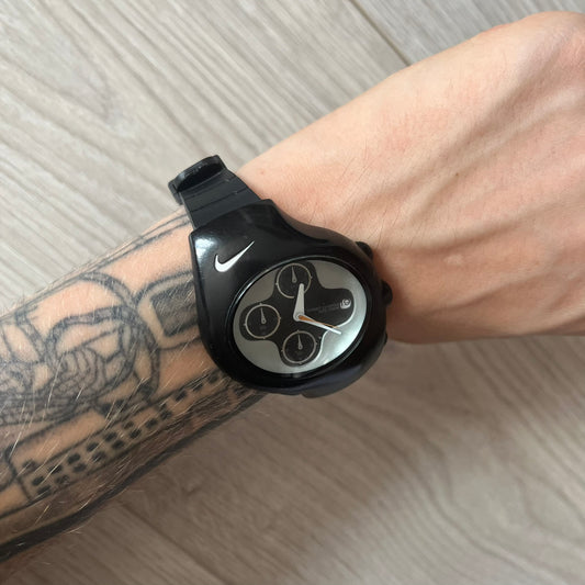 Black Nike watch on a wrist with tattoos, on a light wooden surface