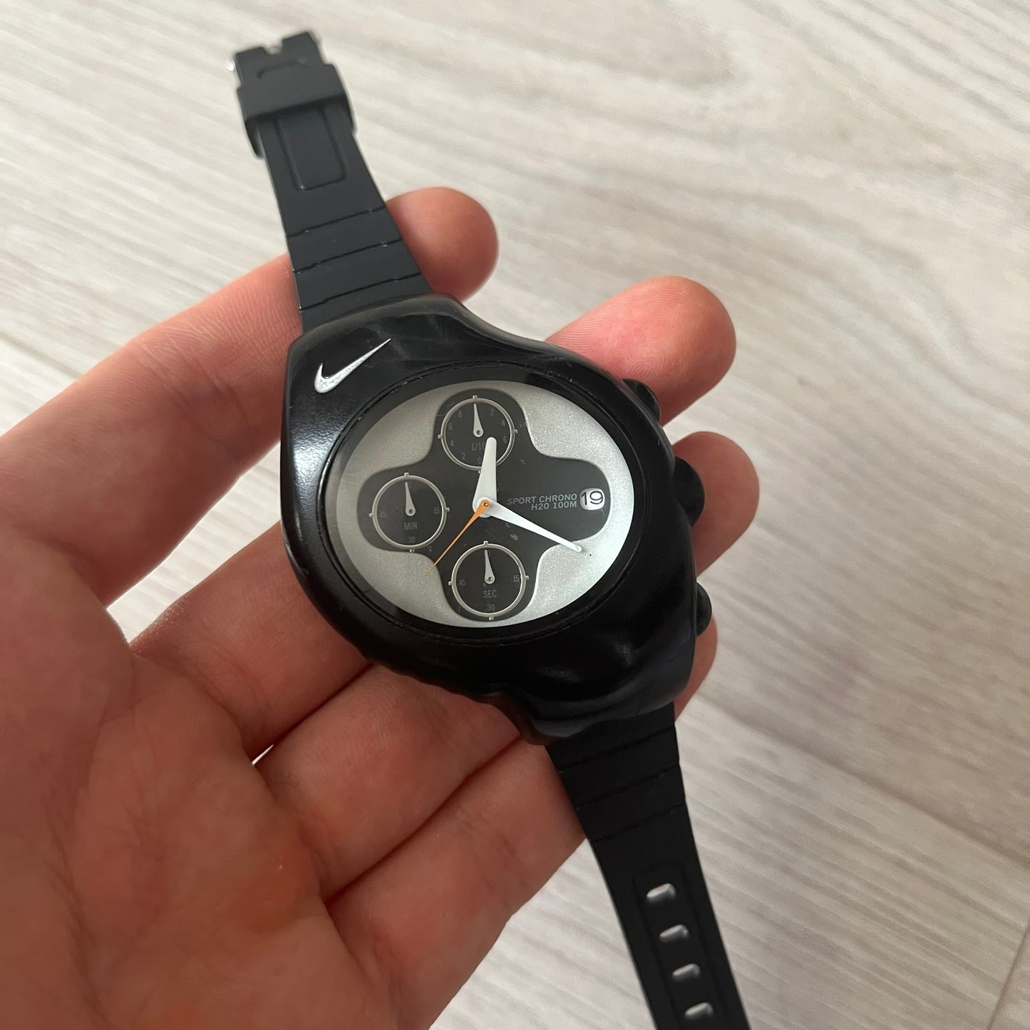 Black wristwatch with a unique face held in a hand on a light background