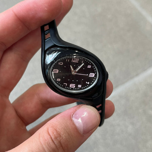 Nike Triax Swift WK0007 Black & Pink Analog Watch features a black rubber strap with matching front case. The black dial has pink hour markers, and silver hands. Small Pink Nike logo sits above the case. Built with stainless steel and metal components, the watch is water resistant up to 50 meters.