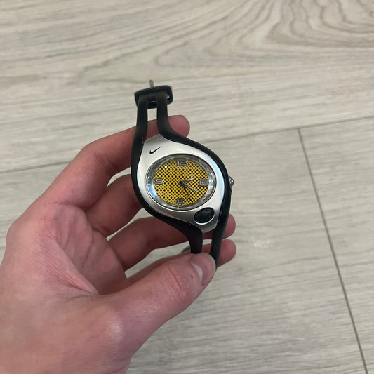 Nike Triax Swift WR0078 analog wristwatch with black rubber straps and a matching rubber outer case. The internal case is silver-tone metal, fitted with a black side button and black Nike Swoosh branding. Features a yellow dotted dial with silver hands and markers, paired with an integrated turquoise backlight that illuminates the face when activated. Sport-oriented construction with a clean, functional layout typical of early-2000s Nike Triax models. 