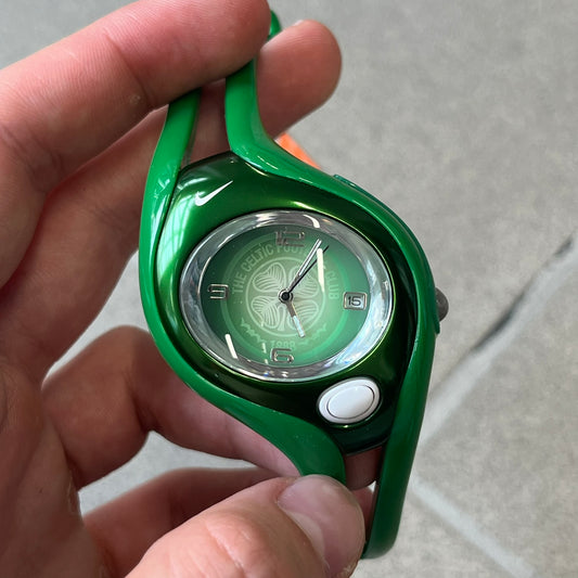 Nike Triax Swift 'Celtic F.C.' WR0078 Green Analog Watch featuring green rubberized straps and a matching green outer shell covering the metal case. The inner case is metallic green with a white light button and a Nike Swoosh on the top. The dial has a light green gradient finish with a large Celtic F.C. crest in the center, visible depending on light angle. Analog display with an integrated turquoise backlight that illuminates the dial.