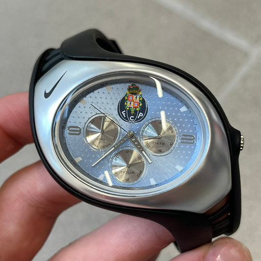 Nike Triax 'FC Porto' Swift 3i WR0091 Analog Watch with black rubber straps and a silver-tone case featuring a black Nike Swoosh at the top. The light blue metallic dial has a recessed dotted texture, FC Porto crest at the top and three silver subdials for day, date, and hour. Seconds markings are printed on the inner edge of the case and are visible only at an angle. 
