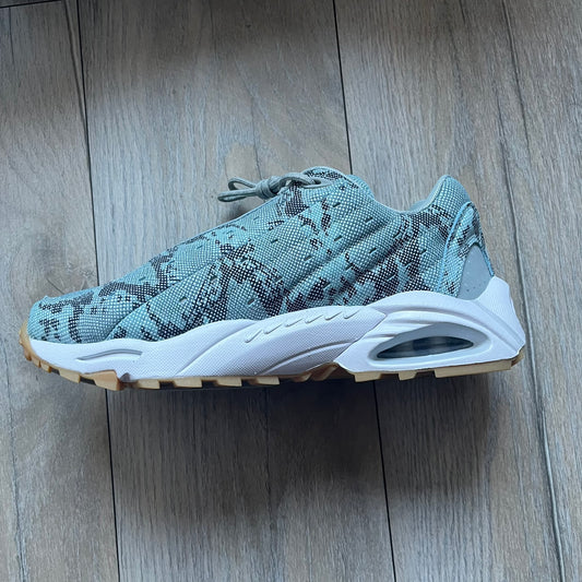 The Nike x NOCTA Hot Step Air Terra “Snakeskin” Light Pumice Sneakers feature a low-top build with a faux snakeskin-textured upper in light pumice blue and grey tones. Details include small 3D mini Swooshes on the sides, reflective piping around the eyestay, oval perforations at the midfoot with a reflective underlay, and NOCTA branding on the tongue and insole. Finished with a white foam midsole inspired by the Air Terra Humara with Zoom Air in the forefoot, a visible Max Air unit in the heel, and a gum ru