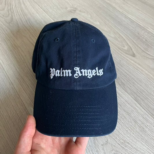 Palm Angels Classic Logo Navy Baseball Cap crafted from 100% cotton. Features white embroidered Palm Angels logos on the front and back in gothic-inspired lettering. A timeless streetwear accessory with a clean navy finish.