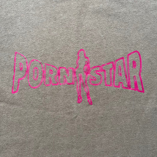 Vintage 90’s Porn Star Clothing longsleeve in brown, featuring a bold pink logo on the chest with a silhouette outline of a woman between the words “Porn” and “Star.” Crafted with quality construction, it carries the brand’s signature edgy aesthetic. Finished with a playful “must be 18 or over” detail on the tag, this rare piece embodies 90’s streetwear provocative style.