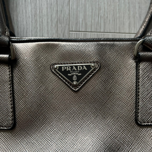 Vintage Prada Metallic Saffiano Bauletto Bag crafted from metallic gold saffiano leather embodies vintage elegance and modern luxury. Detailed with gold-tone hardware, dual handles, and original accessories, it’s a testament to Prada’s enduring craftsmanship. A collector’s piece made to shine on any occasion.