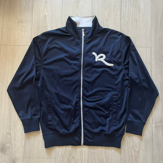 Rocawear Dark Navy Vintage Track Jacket, featuring a small embroidered logo on the chest and a large white logo across the back, finished with a silver emblem near the wrist and a detailed silver zipper.