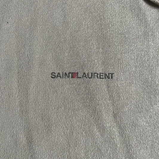 Crafted in France from 100% cotton, this Saint Laurent Beige Hoodie features a minimalist aesthetic with the brand’s signature small Saint Laurent chest logo and red square detail. Designed with a classic front pocket and clean drawstrings without metal tips, it delivers understated Parisian luxury in a neutral tone.