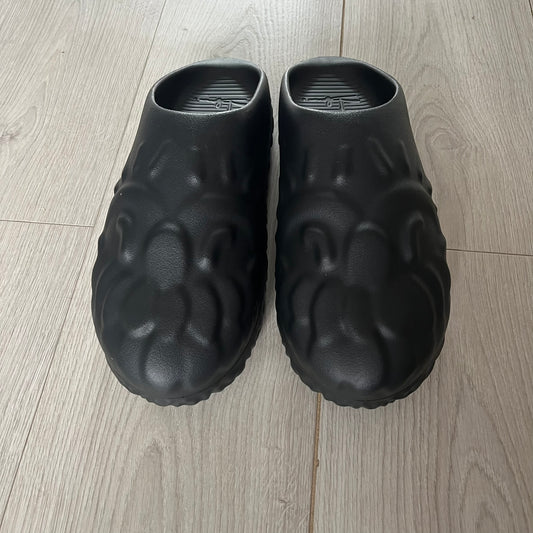 Slawn Shapes Black Chompaz Sliders in the black colorway, designed by artist Olaolu Slawn in collaboration with Shape Shoes. These closed-toe rubber sliders feature Slawn’s signature face design as the body of the shoe. They include a custom tread pattern that leaves a unique footprint. Packaged in a cardboard box with a special plastic bag covered in Slawn’s signature face graphics.