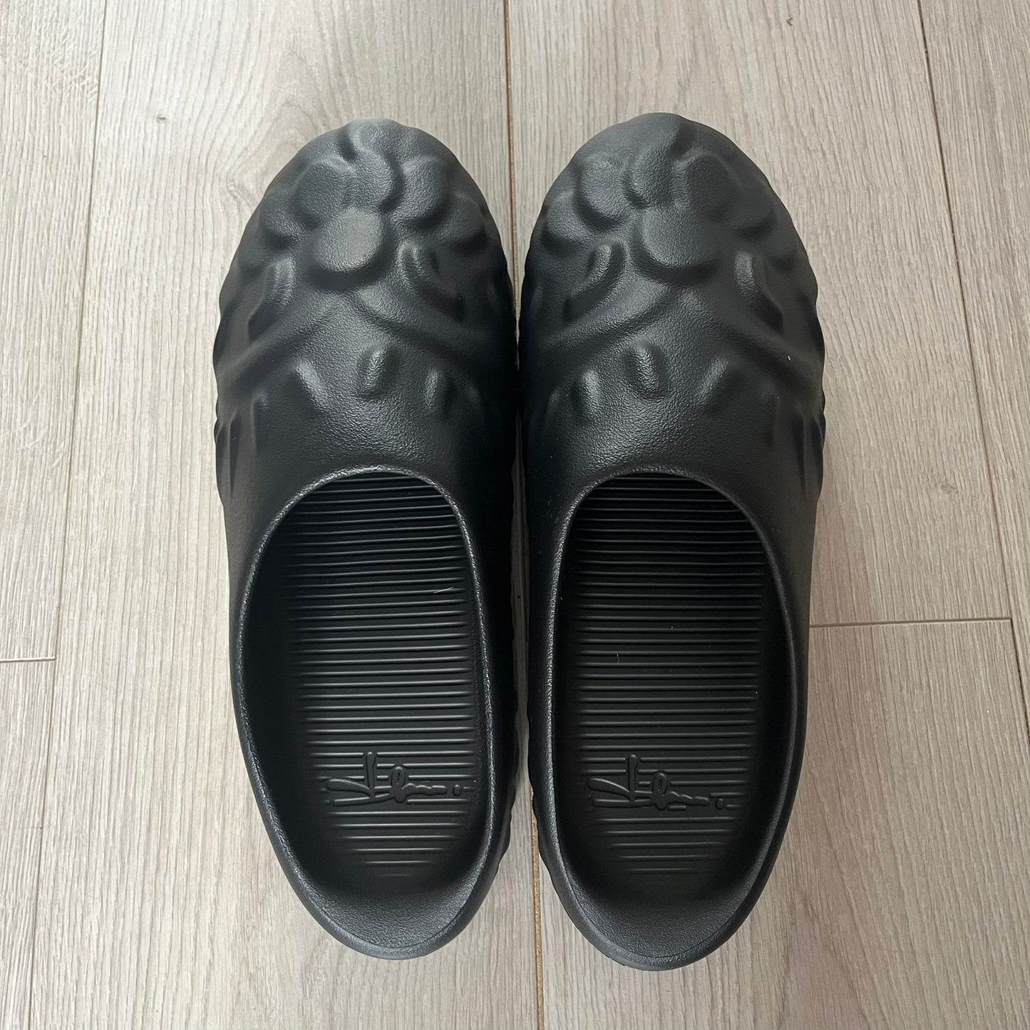 Slawn Shapes Black Chompaz Sliders in the black colorway, designed by artist Olaolu Slawn in collaboration with Shape Shoes. These closed-toe rubber sliders feature Slawn’s signature face design as the body of the shoe. They include a custom tread pattern that leaves a unique footprint. Packaged in a cardboard box with a special plastic bag covered in Slawn’s signature face graphics.