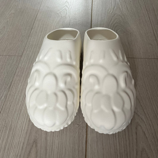 Slawn Shapes Snow Stompaz Sliders in the white colorway, created in collaboration with artist Olaolu Slawn and Shape Shoes. These closed-toe rubber sliders feature Slawn’s signature cartoonish face design forming the body of the shoe and the playful tagline “F*ck Crusty Toes.” The tread is specially designed to leave a unique footprint. They come packaged in a cardboard box filled with snow-like wool and include a special silver sticker.