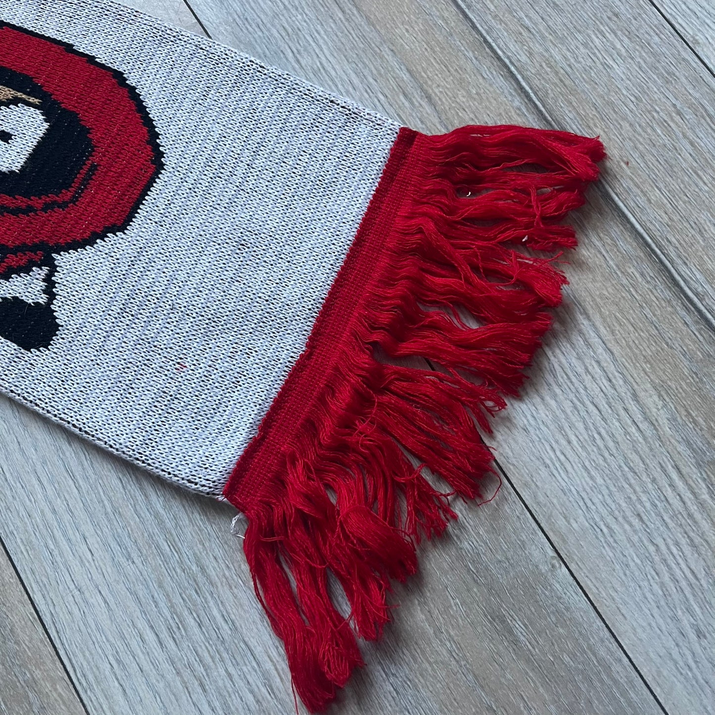 Vintage football scarf in white and black with red fringe / tassels, featuring South Park characters including Kenny, Cartman, and Kyle dressed in Arsenal kits with “Gooners” text. The character graphics appear on both sides of the scarf, with consistent coloring in white and red. Soft knit construction with a classic football scarf shape and finish.