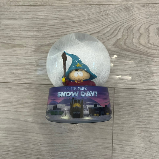 Exclusive South Park Snow Day Grand Wizard Cartman Snowglobe. Showcases Cartman in full wizard attire within a globe packed with dense snow for a humorous effect, making Cartman almost disappear beneath the flakes. Officially licensed piece with 2024 Comedy Partners text on the base.