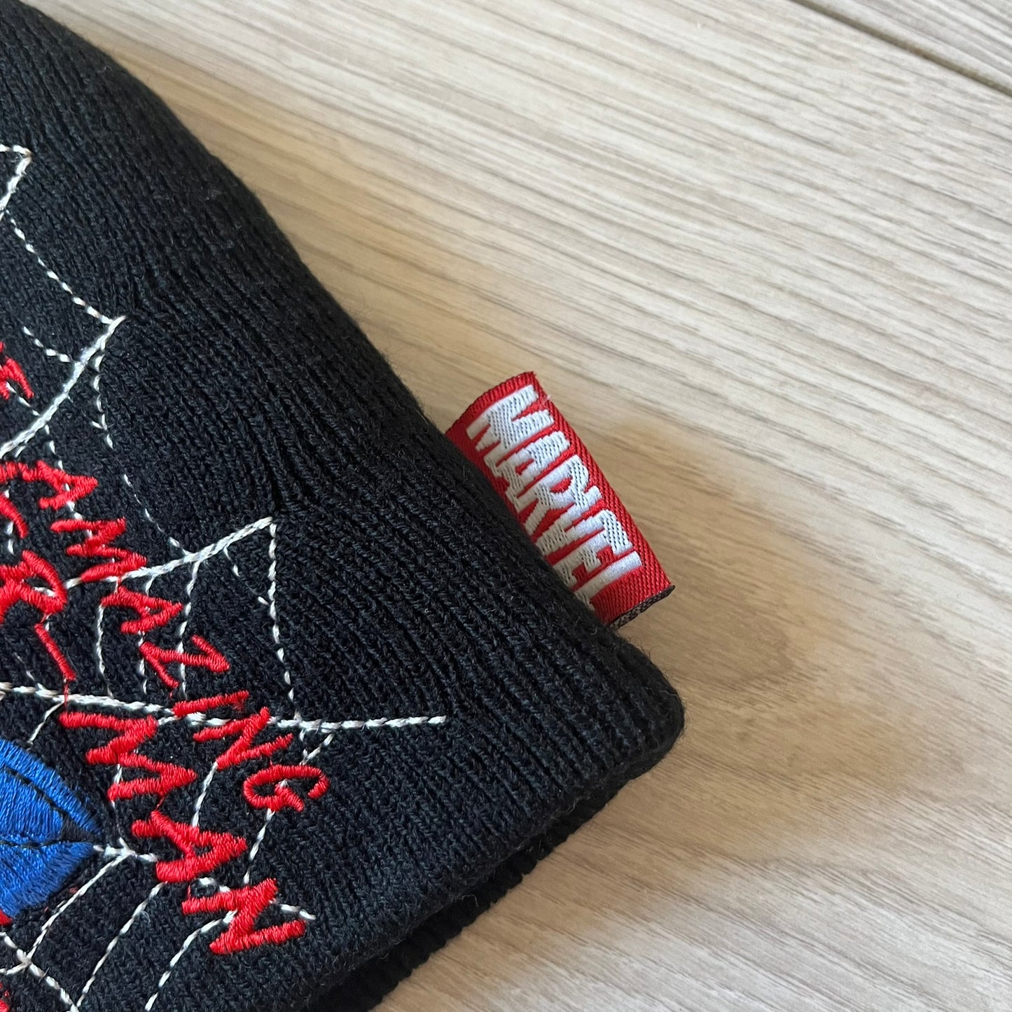 Black Spider-Man glove with red 'Marvel' label on a light wood surface