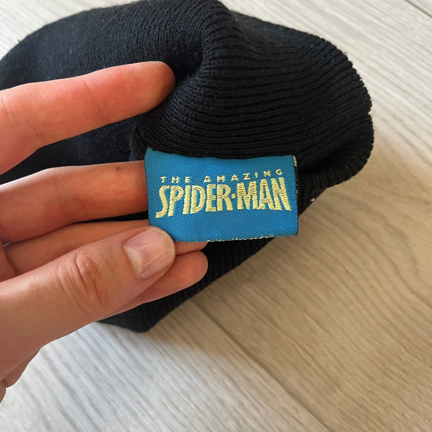 Black sock with 'The Amazing Spider-Man' label held by a hand on a light wooden surface