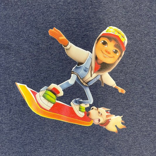 Subway Surfers 2010s Jake Tee is a grey T-shirt made on a Fruit of the Loom blank. The front features Jake, the main character from Subway Surfers, riding his skateboard, with the pursuing guard dog biting the end of the board. The design is printed in full color on the front.