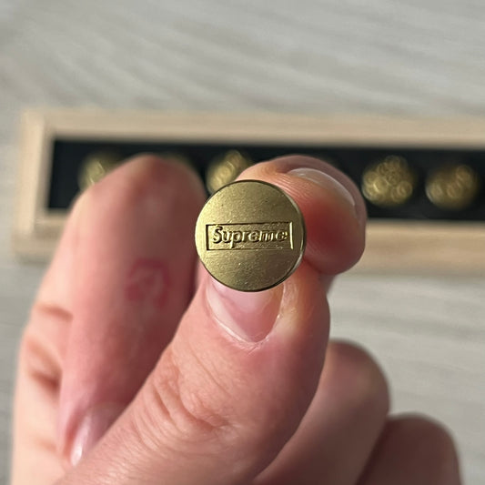 The Supreme CDW Push Pin FW24 Set, released in Week 10 (October 2024), offers eight brass-made pins with detailed debossed graphics including the classic Box Logo and “Fuck Em!” motif. Produced in Japan, this set turns simple desk essentials into collectible Supreme artifacts.