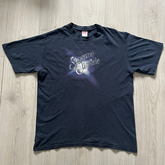 Supreme Clientele FW20 Navy Tee released in October 2020 as part of Supreme’s Fall/Winter 2020 collection. This cotton tee pays tribute to Ghostface Killah’s 2000 album Supreme Clientele, featuring the album’s iconic title graphic on the front and full tracklist on the back. A standout Supreme graphic tee that merges streetwear with hip-hop history.