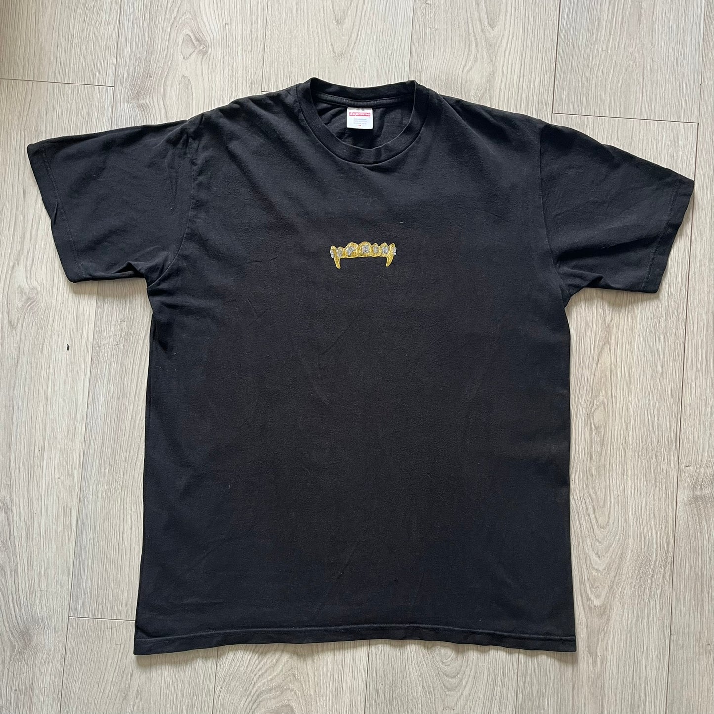 Supreme Fronts SS19 Black Tee released on February 21, 2019, as part of the brand’s Spring/Summer 2019 collection. Crafted from 100% cotton, it features a gold grill design with diamond fangs and a jeweled Supreme logo across the teeth. A standout graphic tee from Supreme’s early SS19 lineup.