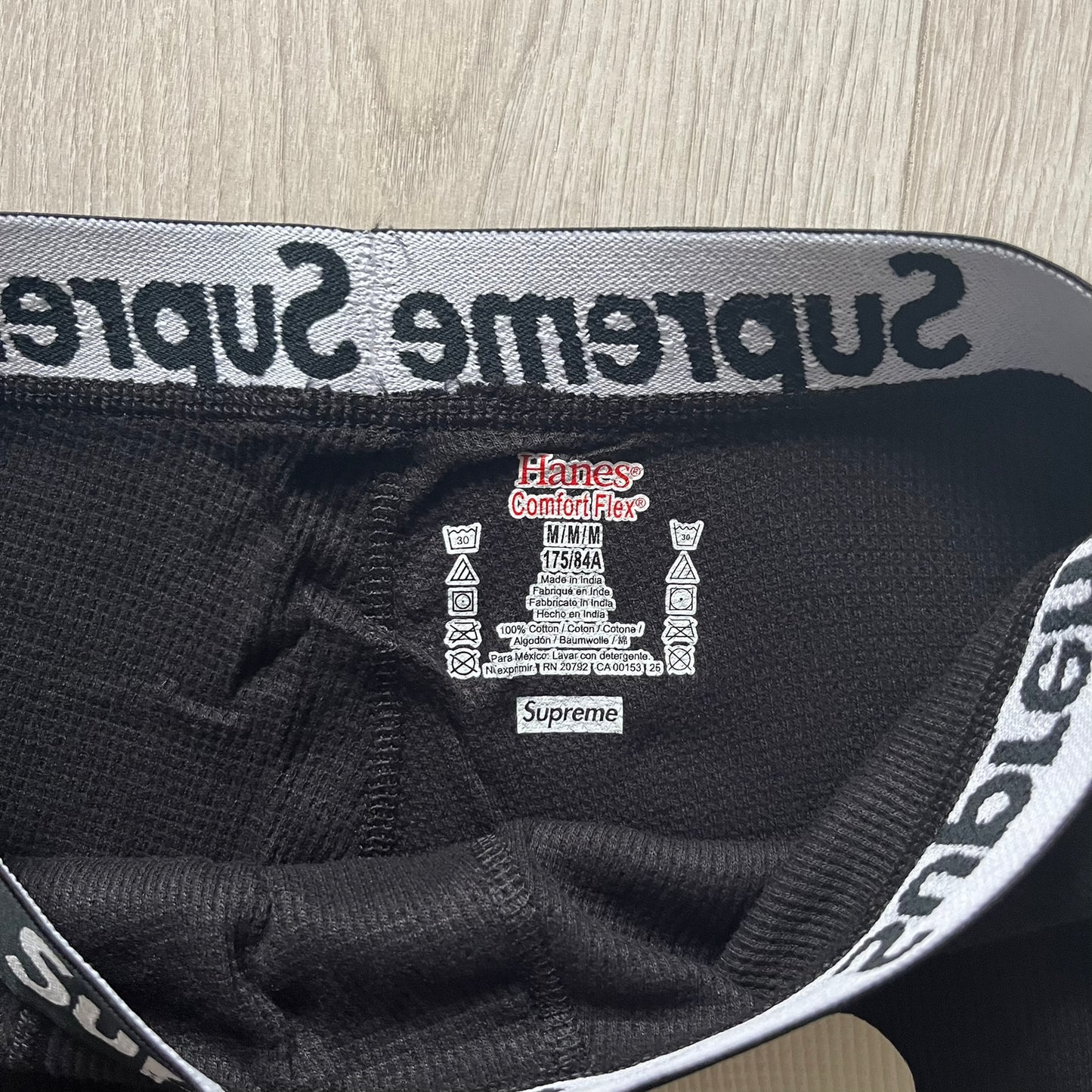 Supreme Hanes Bones Thermal Pant FW25 in black, crafted from 100% cotton. Features white skeletal bone prints running down both legs and a black elastic waistband with white Supreme branding throughout. Released October 23, 2025.