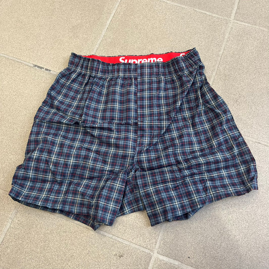 Supreme Hanes FW26 Plaid Boxers feature a plaid pattern and a red Supreme elastic waistband concealed inside. Made from 55% cotton and 45% polyester with Hanes Comfort Flex construction. Pink, grey, blue, and yellow colorways.