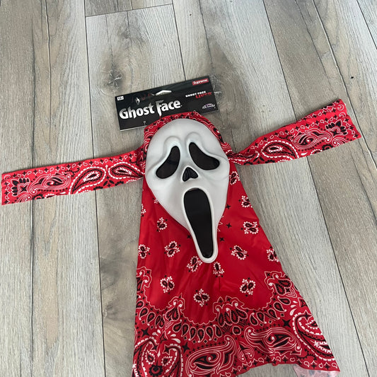 Supreme SS26 Ghostface Mask is a PVC face mask released on April 30, 2026, as part of the Spring/Summer 2026 collection. The mask features the classic white Ghostface design, combined with a red fabric hood element covered in white and black bandana-style patterns and integrated Supreme tags. Additional hanging strips on the sides enhance the hooded visual effect.