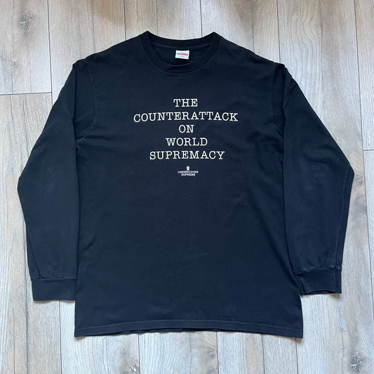 Supreme Undercover Public Enemy Counterattack SS18 Longsleeve Tee is a black long-sleeve T-shirt released on March 15, 2018, crafted from 100% cotton. The front features white “The Counterattack On World Supremacy” text with a small Supreme UNDERCOVER logo beneath, while the back displays a large Public Enemy “Fear of a Black Planet” graphic with galaxy and planet imagery and the same co-branded logo below. The design includes a ribbed crewneck and ribbed cuffs, reflecting the SS18 collaboration between Sup