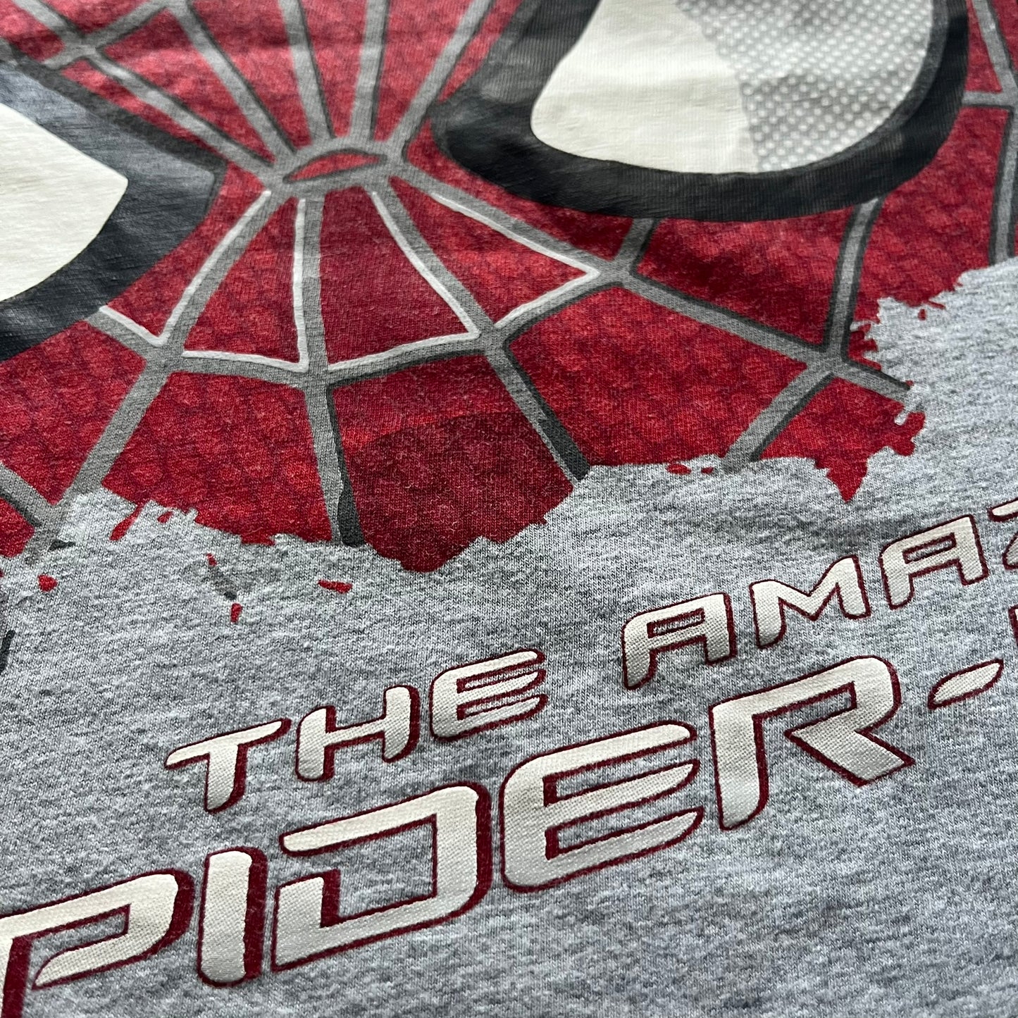 Gray 2014 Marvel tee featuring The Amazing Spider-Man 2 design with a “ripped page” effect showcasing Spider-Man’s face in the center. Text logo sits beneath the graphic for a bold cinematic touch. A collectible piece from the official movie merchandise line.